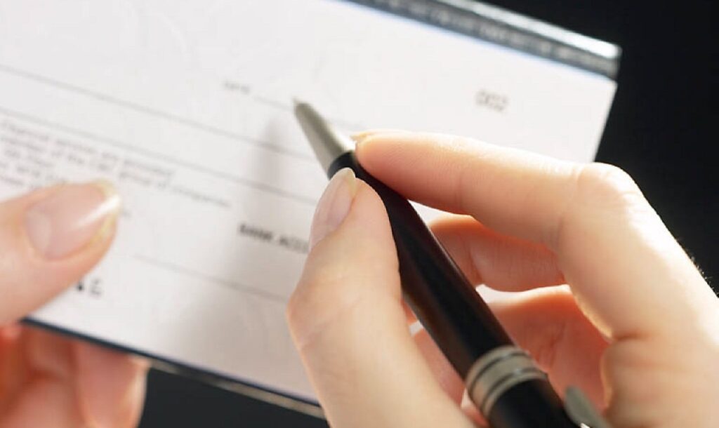 Mano con bolígrafo escribiendo sobre un cheque