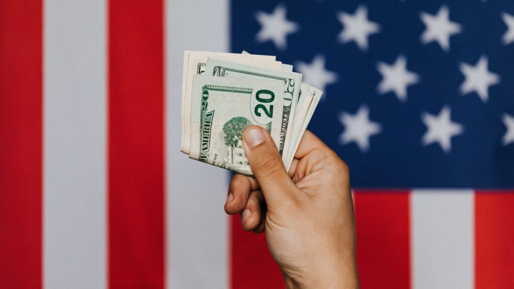 Mano con dinero y bandera de EEUU alude a ingresos determinan acceso a ayudas