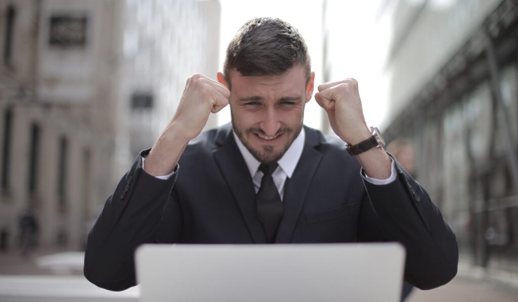 Hombre frente a laptop con manos arriba celebrando su exito en trabajo-dinero en EEUU